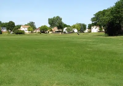 a large grassy field with houses in the background