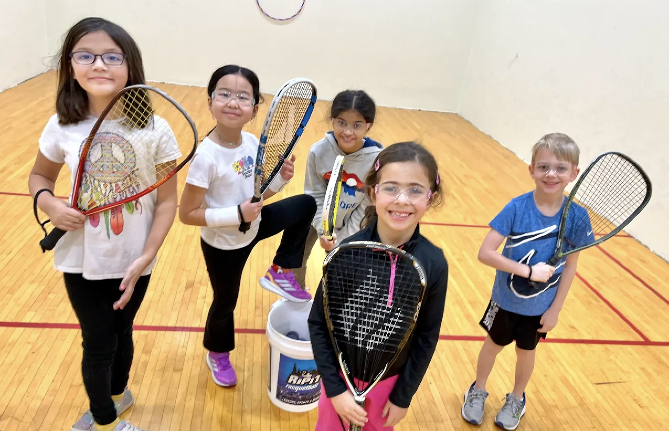 a group of kids in raquetball court holding raquets